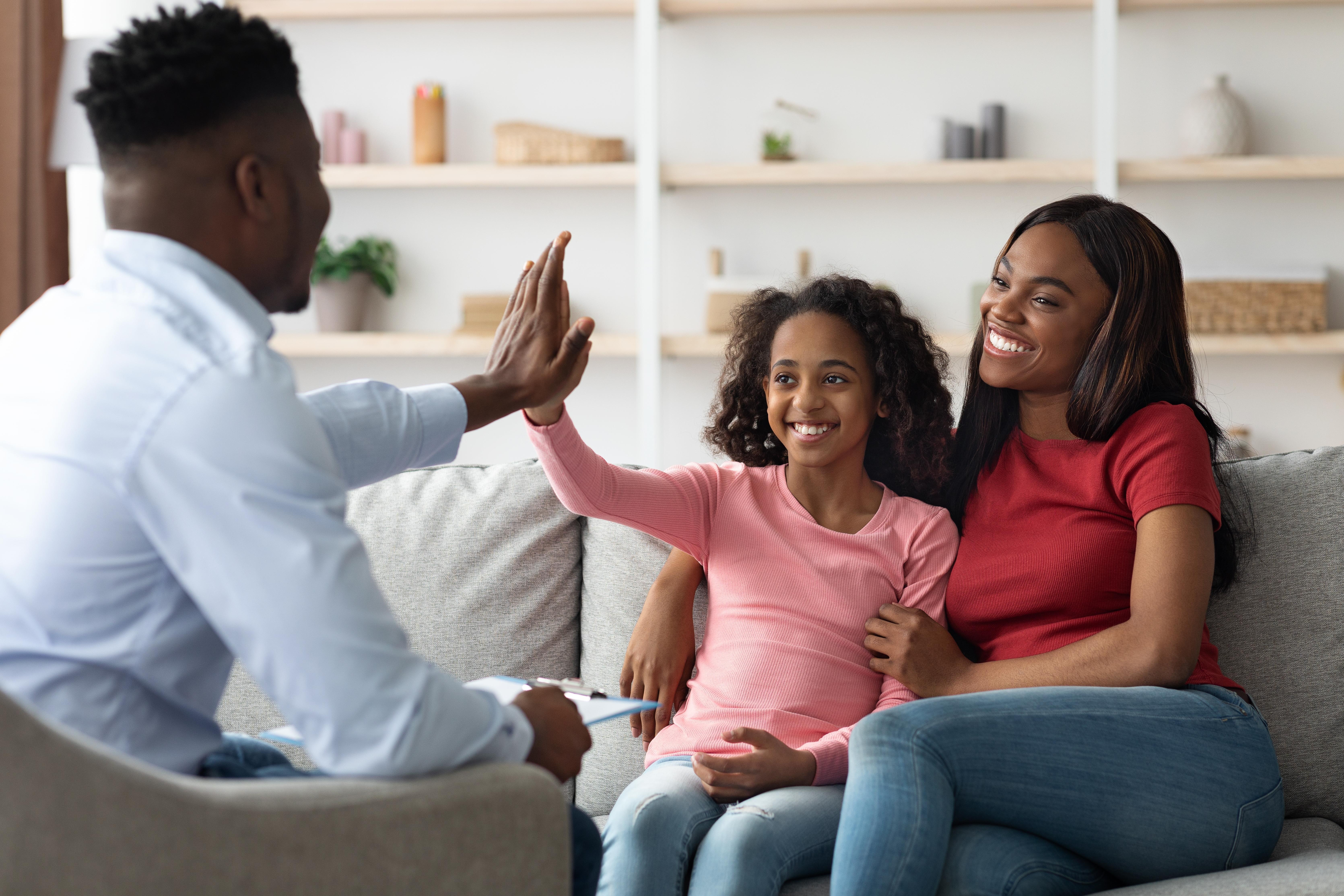ABA therapist giving a high-five to a smiling child seated beside her mother